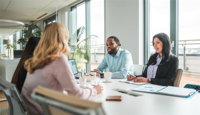A group of four individuals sitting at a conference table in an office having a business meeting.